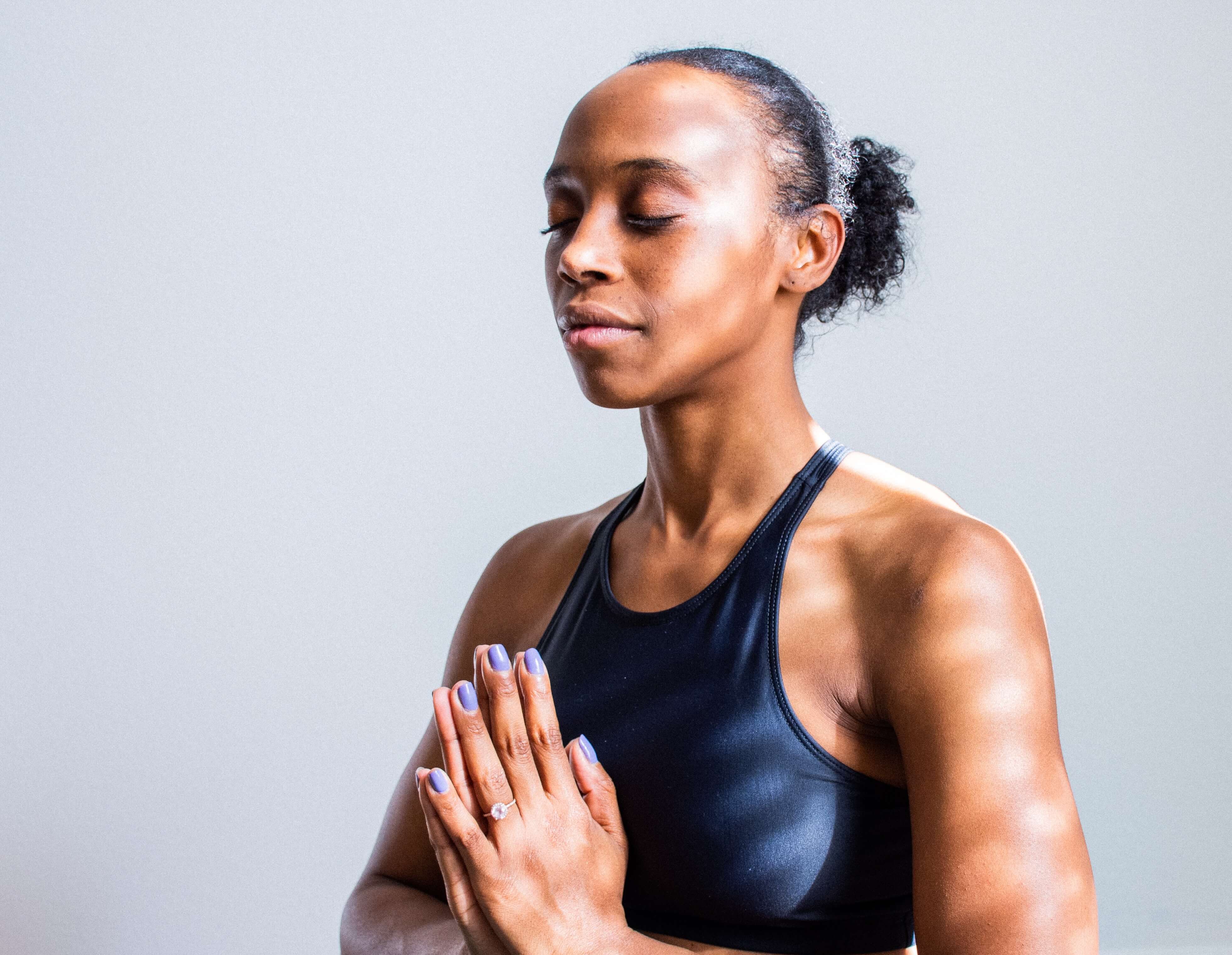 black woman sitting with palms together at chest meditating