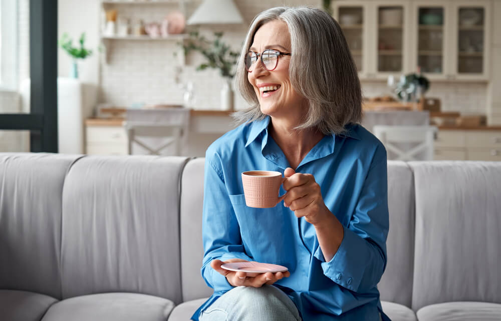 woman with grey hair sitting on couch with tea